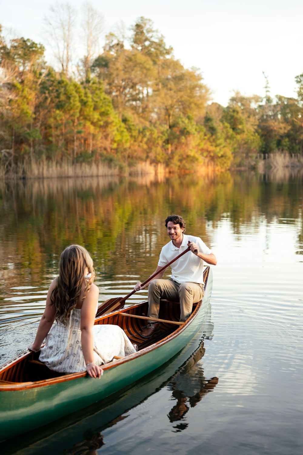 Couple paddling together in a green canoe on a serene lake surrounded by autumn trees at sunset.