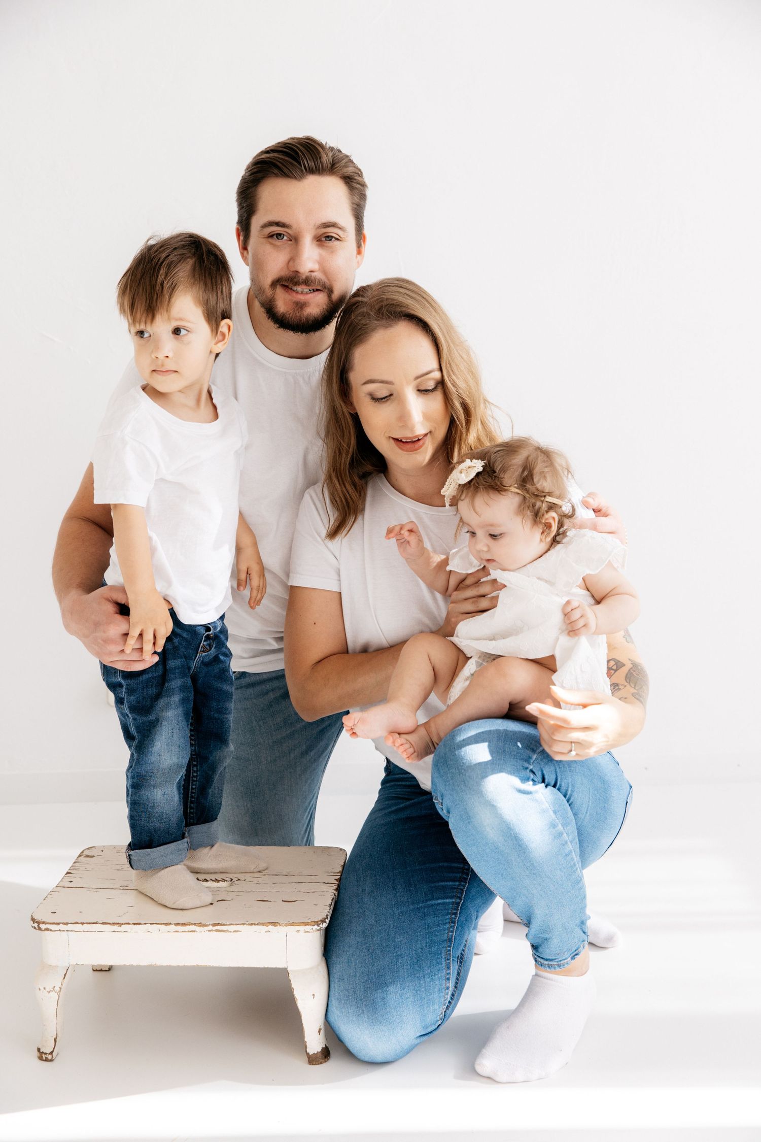 Family portrait of parents with two young children on white bench.