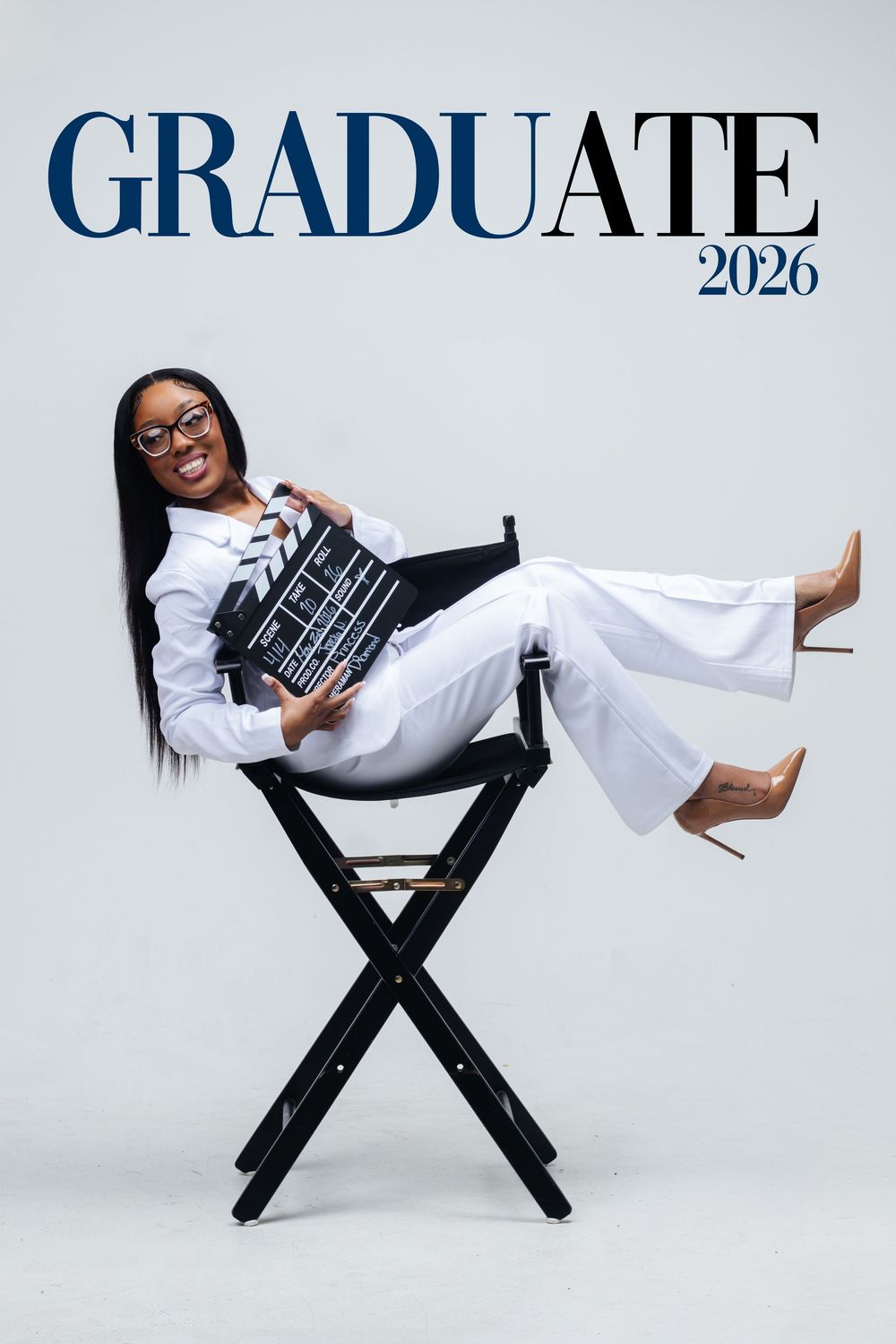 A smiling graduate in white outfit sits in director's chair holding a clapperboard, Graduate 2026 text overlay.