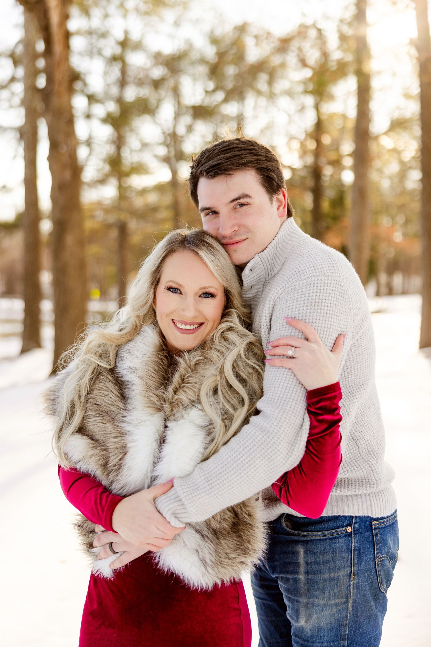 A couple embraces while wearing winter attire in a snow-covered forest setting.