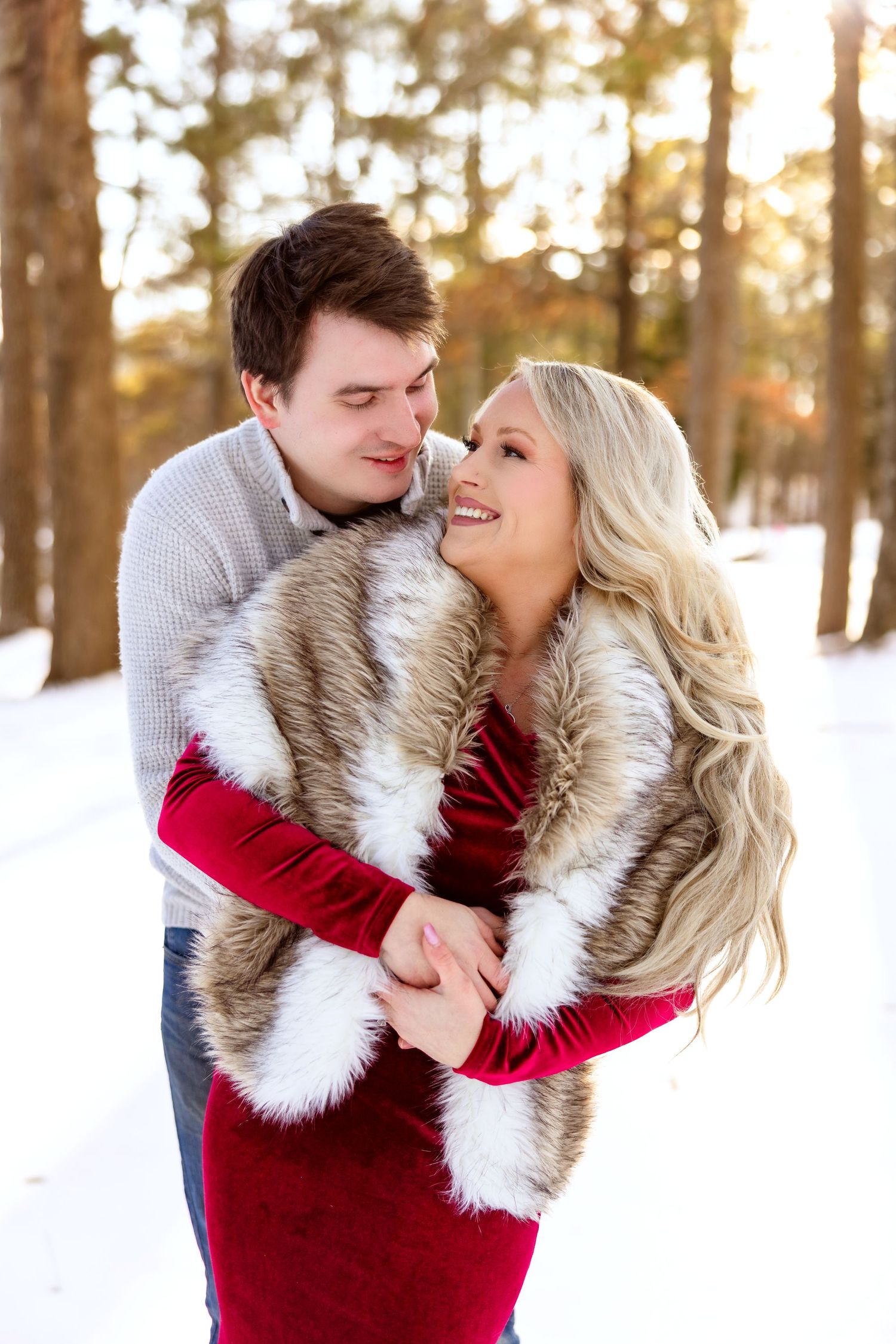 A romantic winter portrait of a couple laughing together in a snowy forest setting.