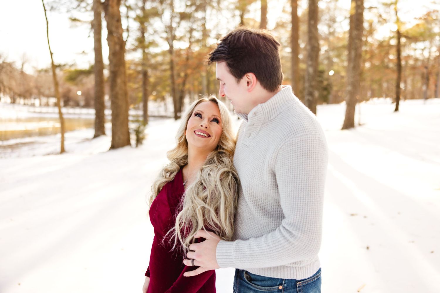 A romantic couple shares a joyful moment together in a snowy winter forest setting at sunset.