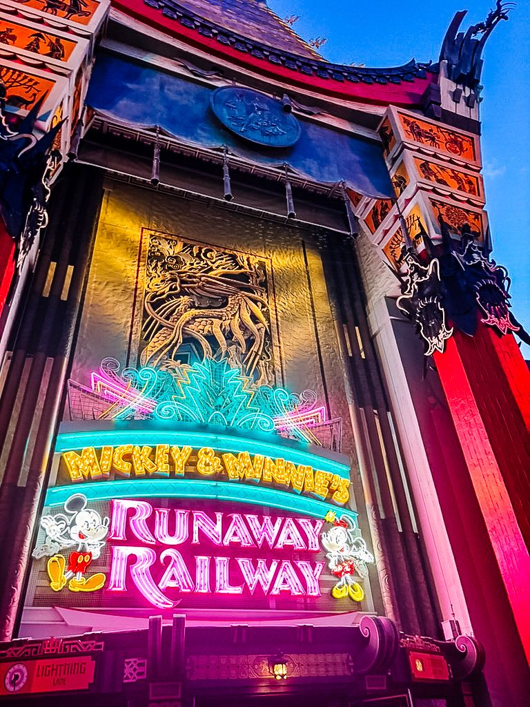Colorfully illuminated neon signs for Mickey & Minnie's Runaway Railway attraction glowing against a dark building facade.