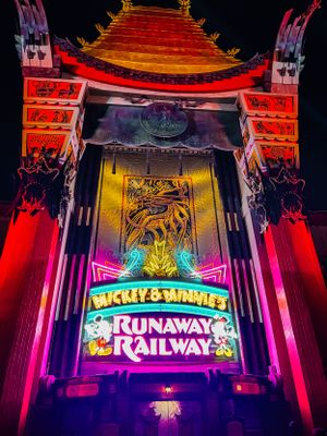 Illuminated neon signs of Mickey & Minnie Runaway Railway attraction with vibrant red and pink lighting at night.