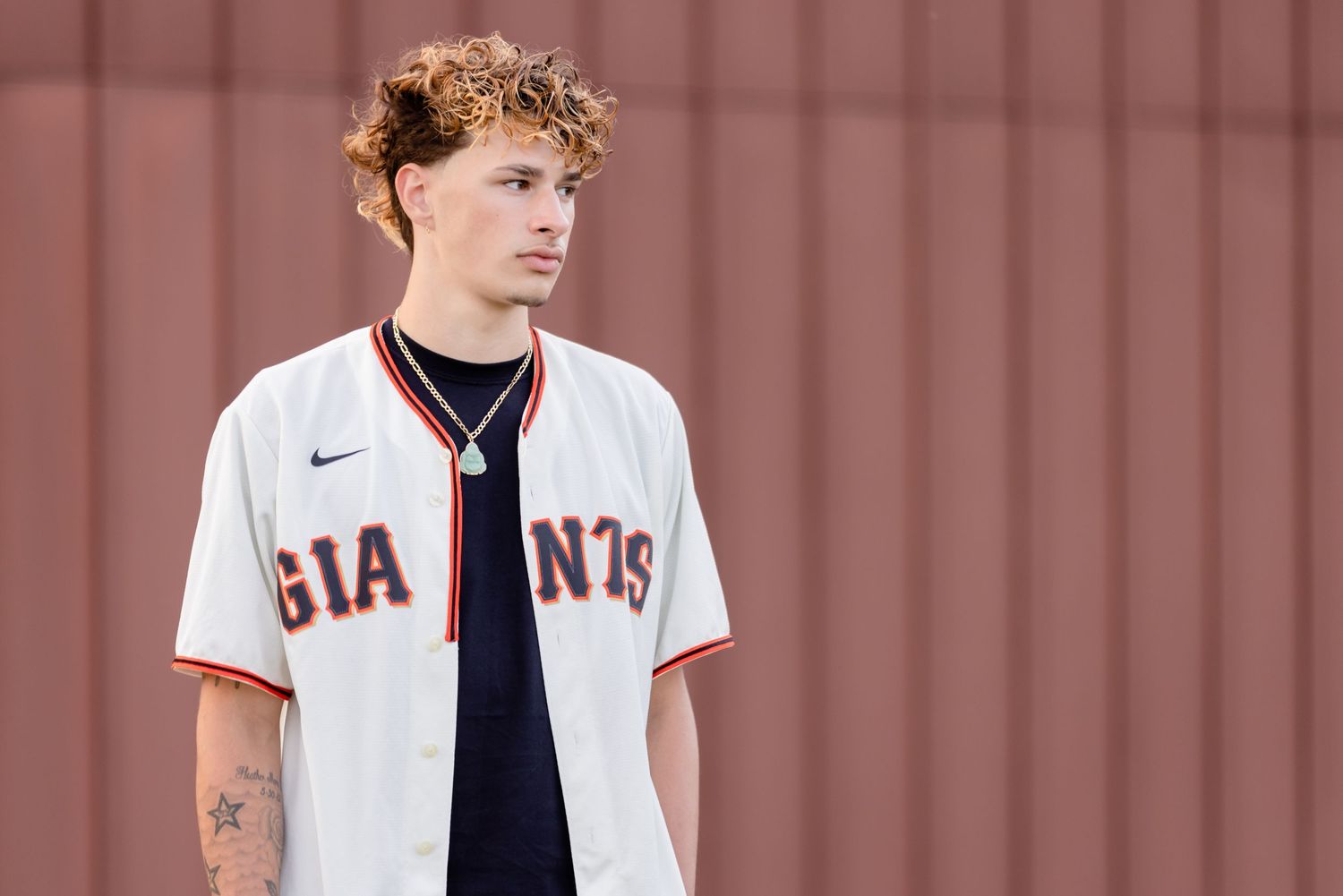 Baseball player in white San Francisco Giants home jersey poses against orange wall.