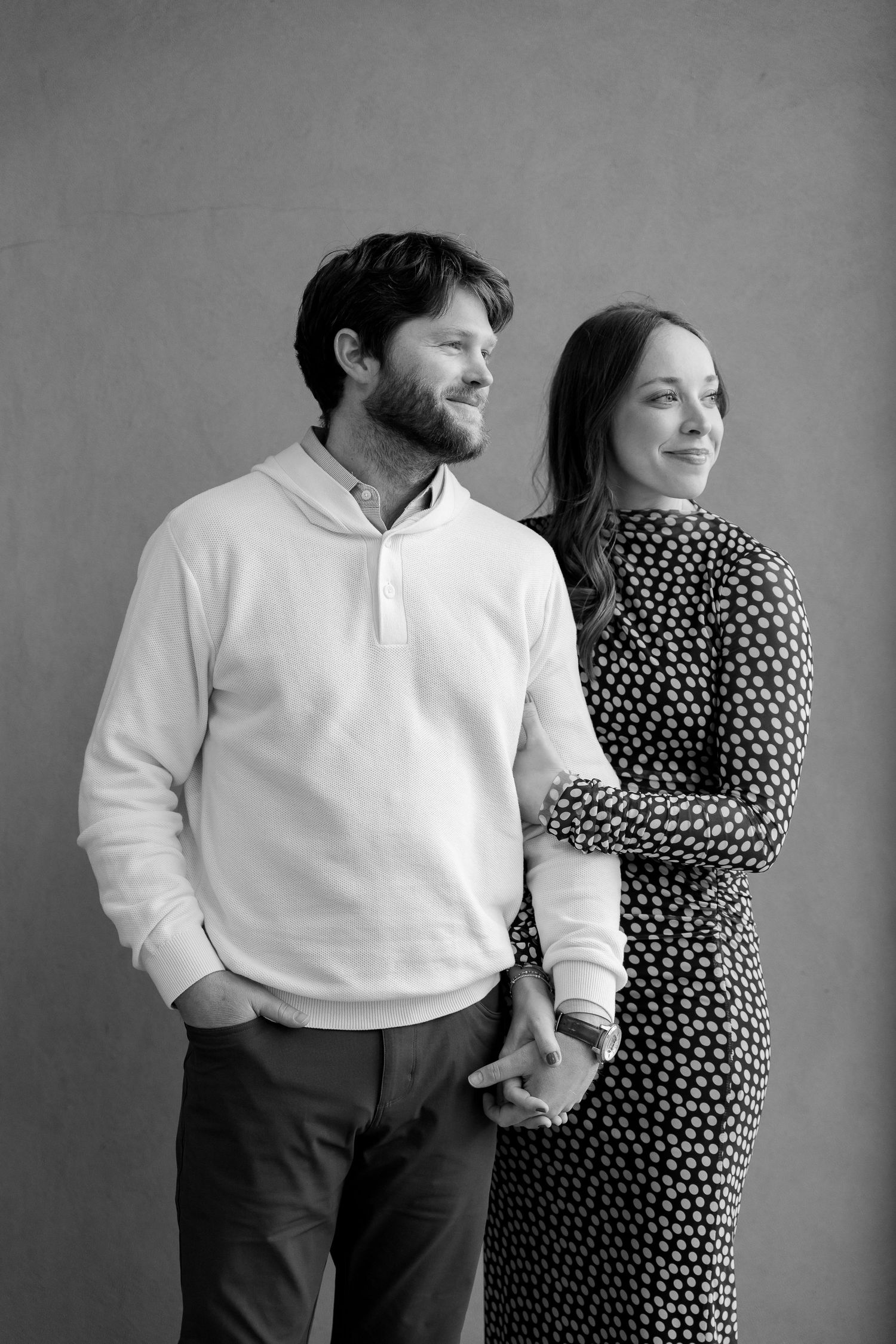 A couple stands close together in a romantic black and white outdoor forest setting with sunlight filtering through trees.