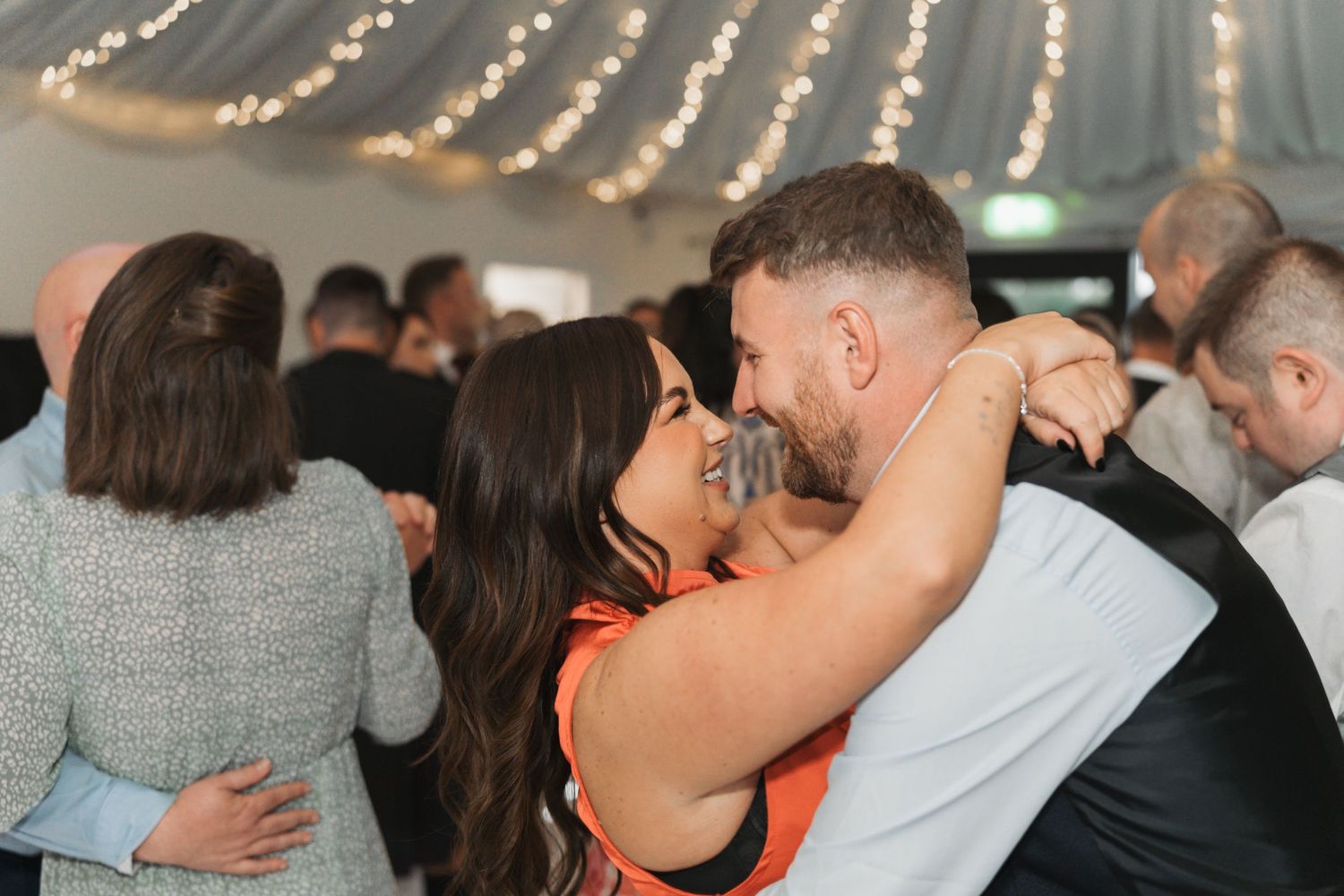 Couple sharing an intimate dance moment under decorative lights at an indoor reception venue.