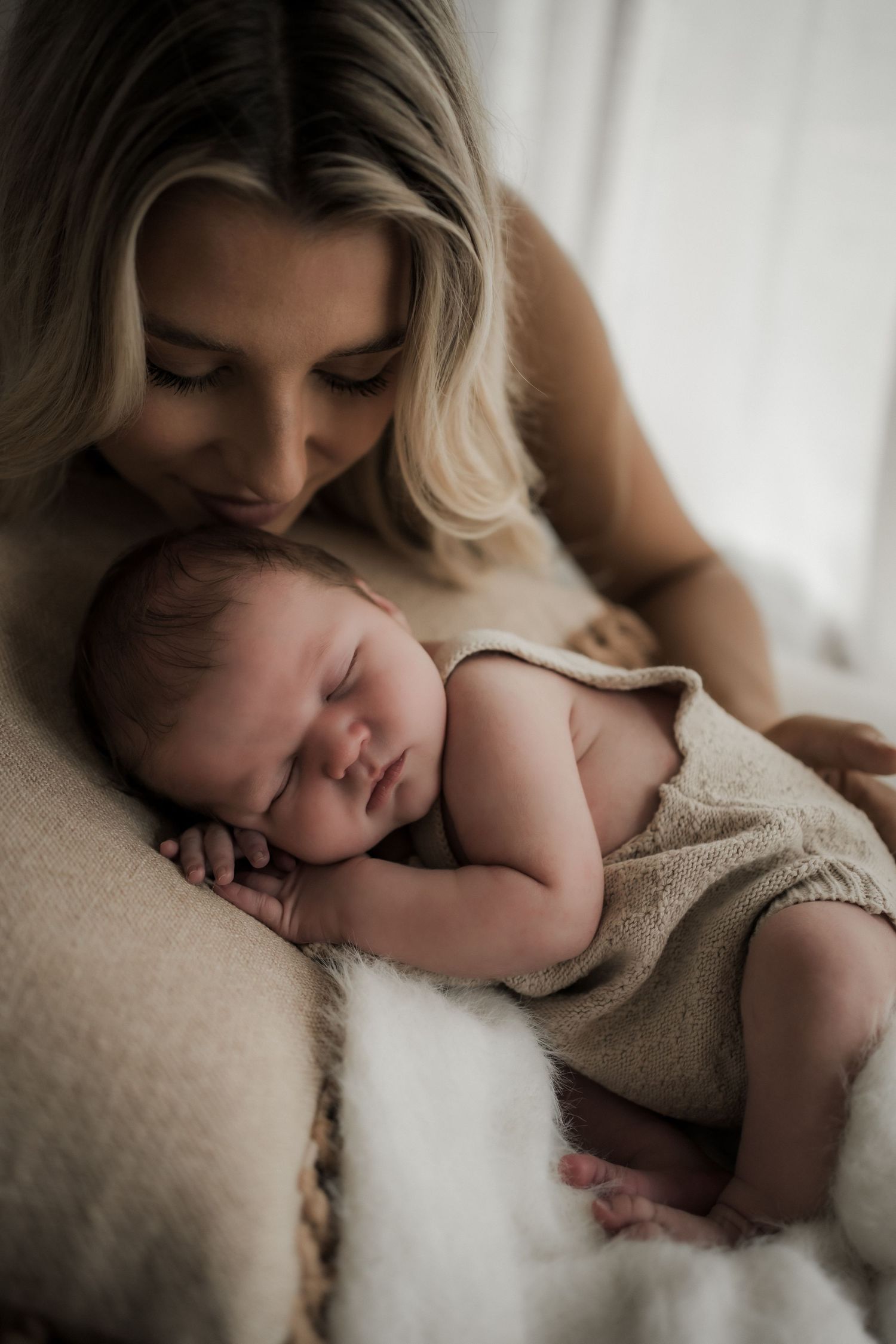 Tender moment between parent and newborn by window in soft natural light.