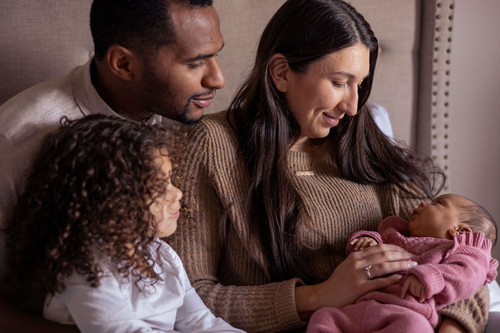 Mom, dad, and toddler girl look at newborn girl.