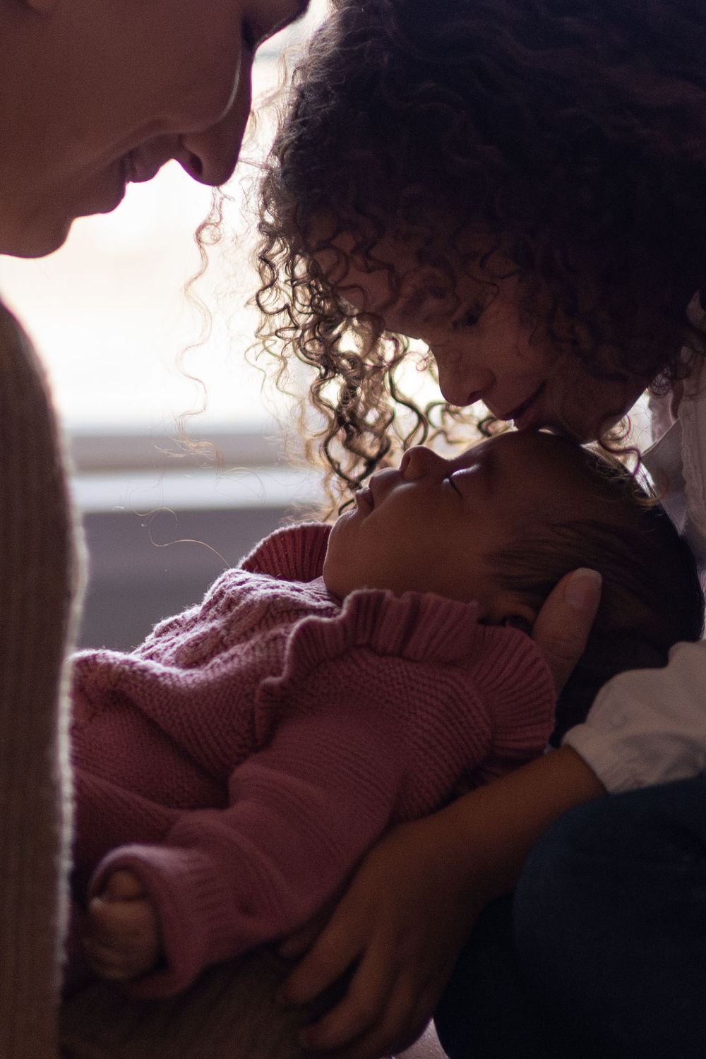 A mom watches as her daughter kisses the top of her newborns head.