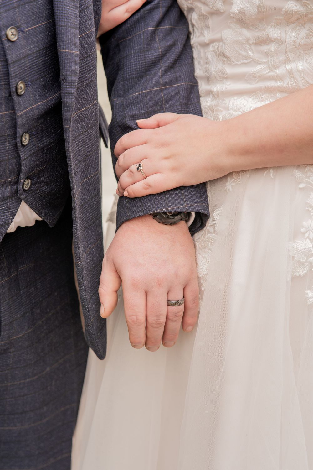 Close-up of newlyweds' hands showing their wedding rings against formal attire.