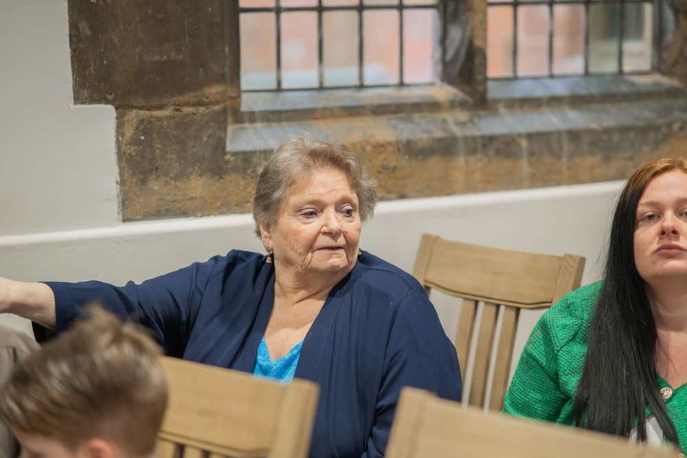 Guests seated on wooden chairs during an indoor celebration event.