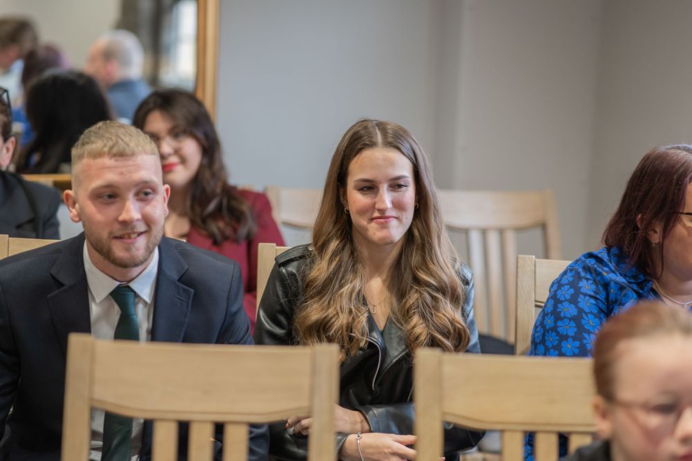 Wedding guests sitting in wooden chairs smiling during indoor ceremony celebration.