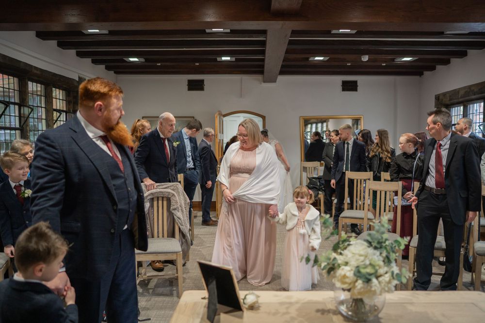 Wedding guests gathered in an indoor venue with rustic wooden beams and elegant floral decorations.