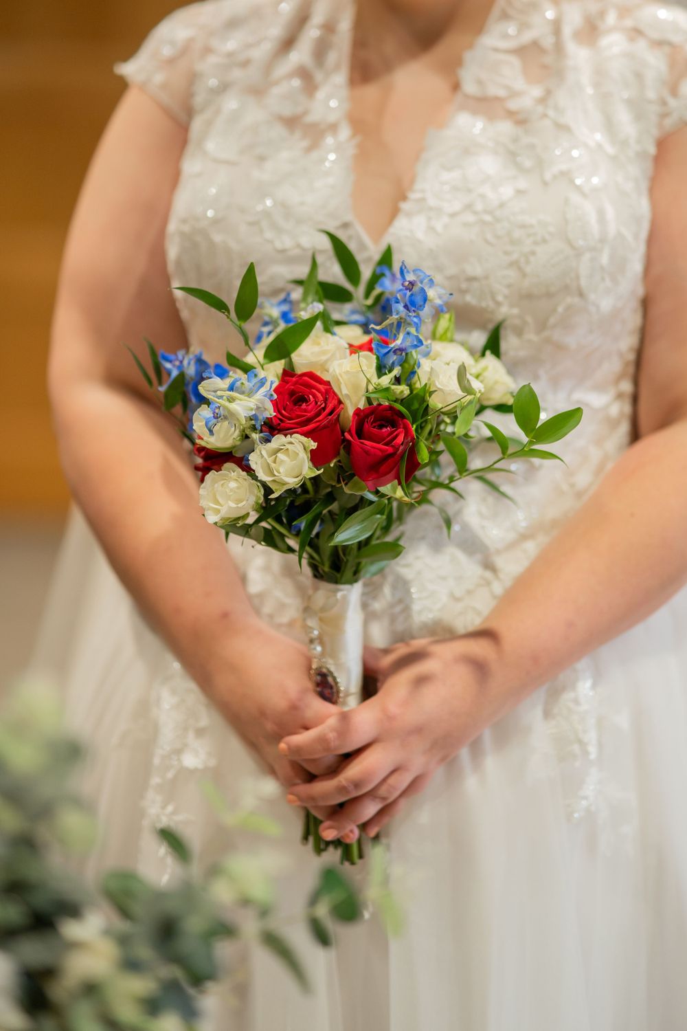 Close-up of a wedding bouquet with red roses, white flowers and blue delphinium held by the bride.