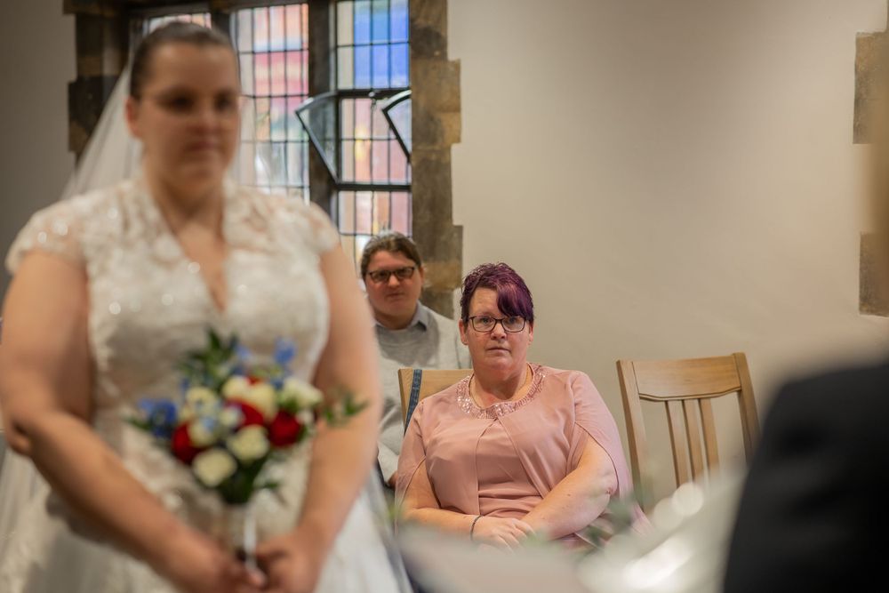A wedding ceremony scene in a church with seated guests and a bride holding a colorful flower bouquet.