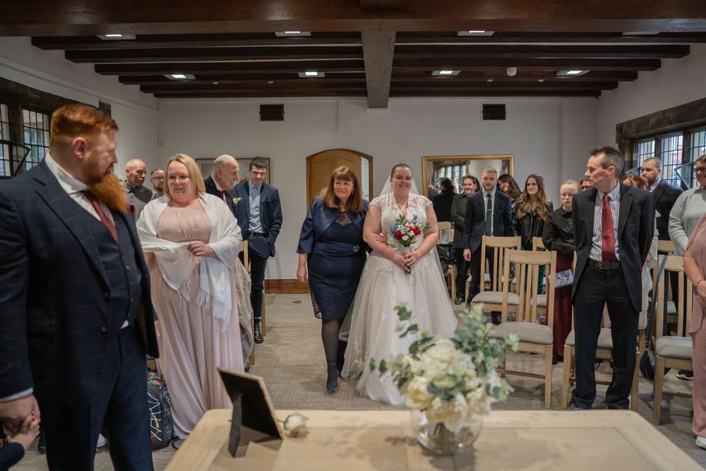 Wedding ceremony attendees gather in a rustic indoor venue with wood beams and floral decorations.