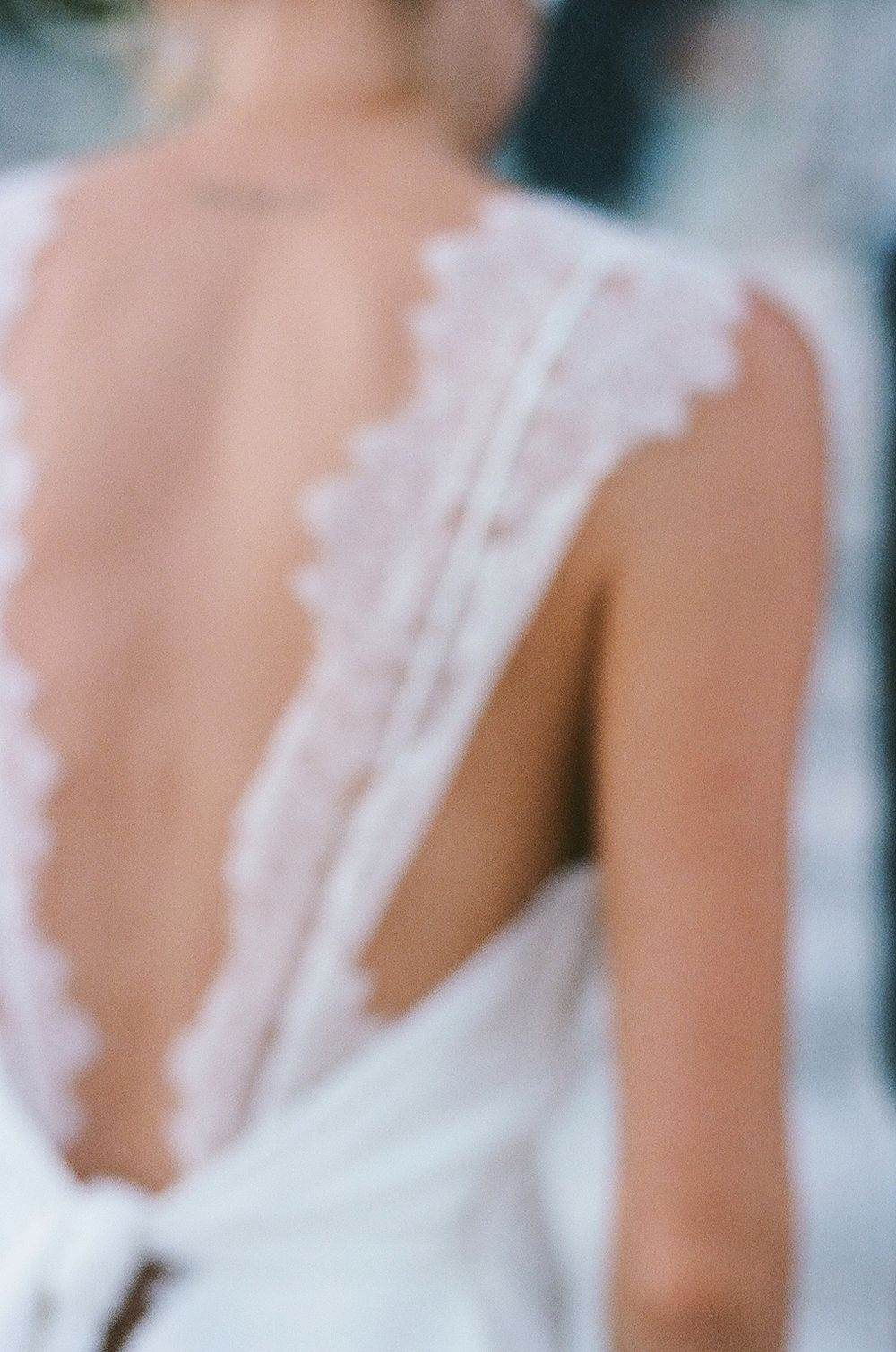 Soft focus detail of a delicate white lace wedding dress by Savannah Miller showing an open back design.
