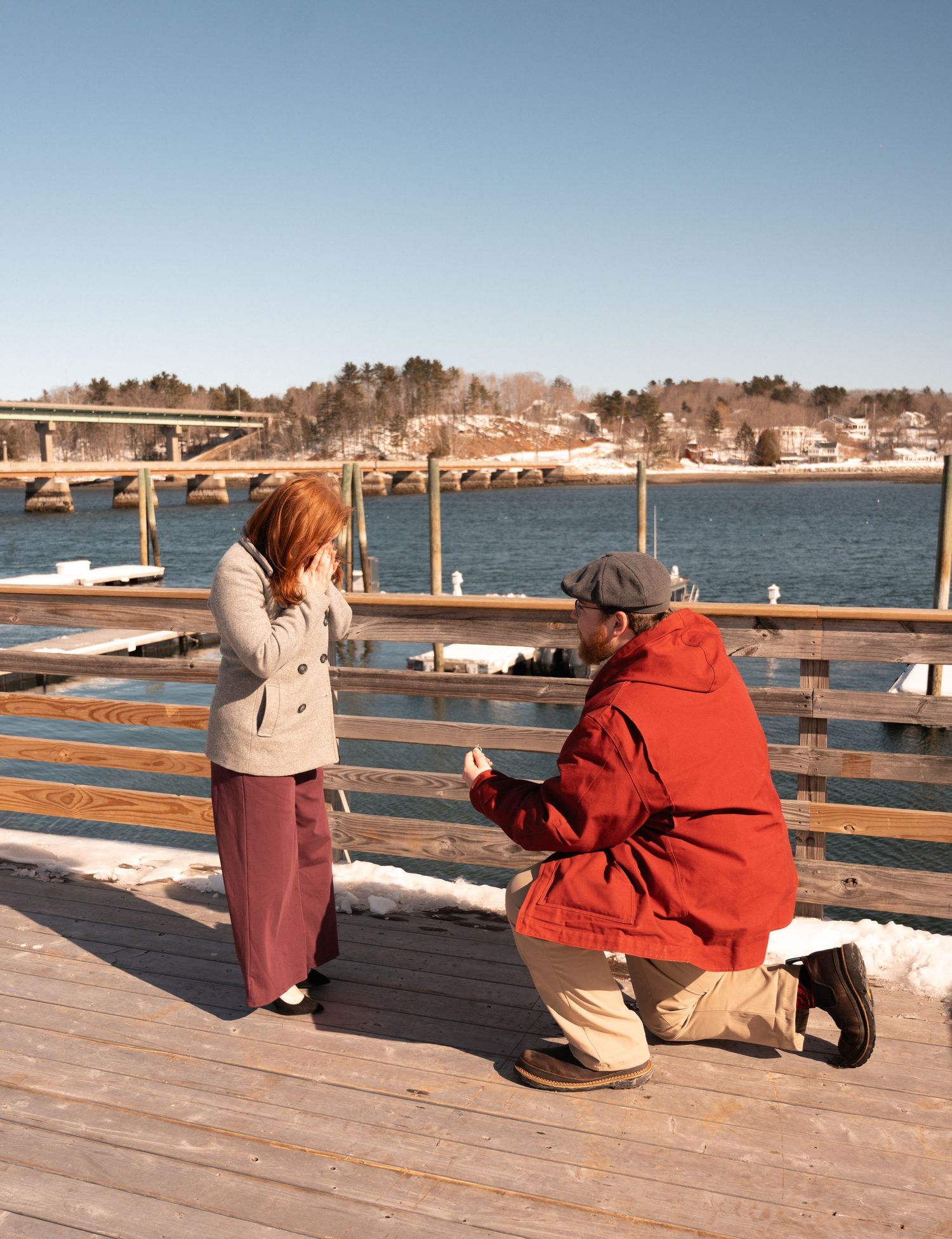 A proposal on a wooden pier overlooking a scenic waterfront view on a sunny day.