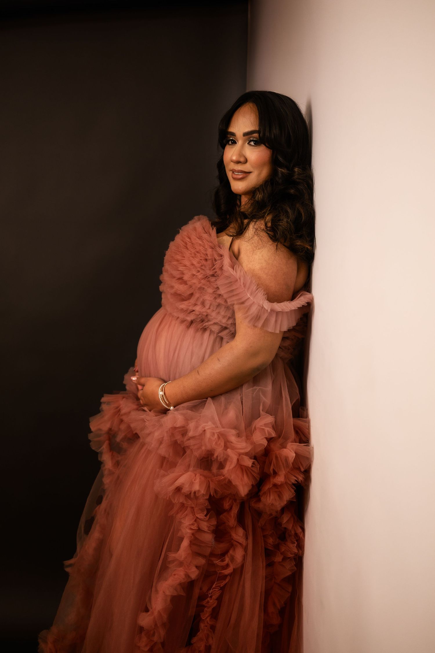 Elegant maternity portrait in pink tulle gown against dark studio backdrop in Goodyear.