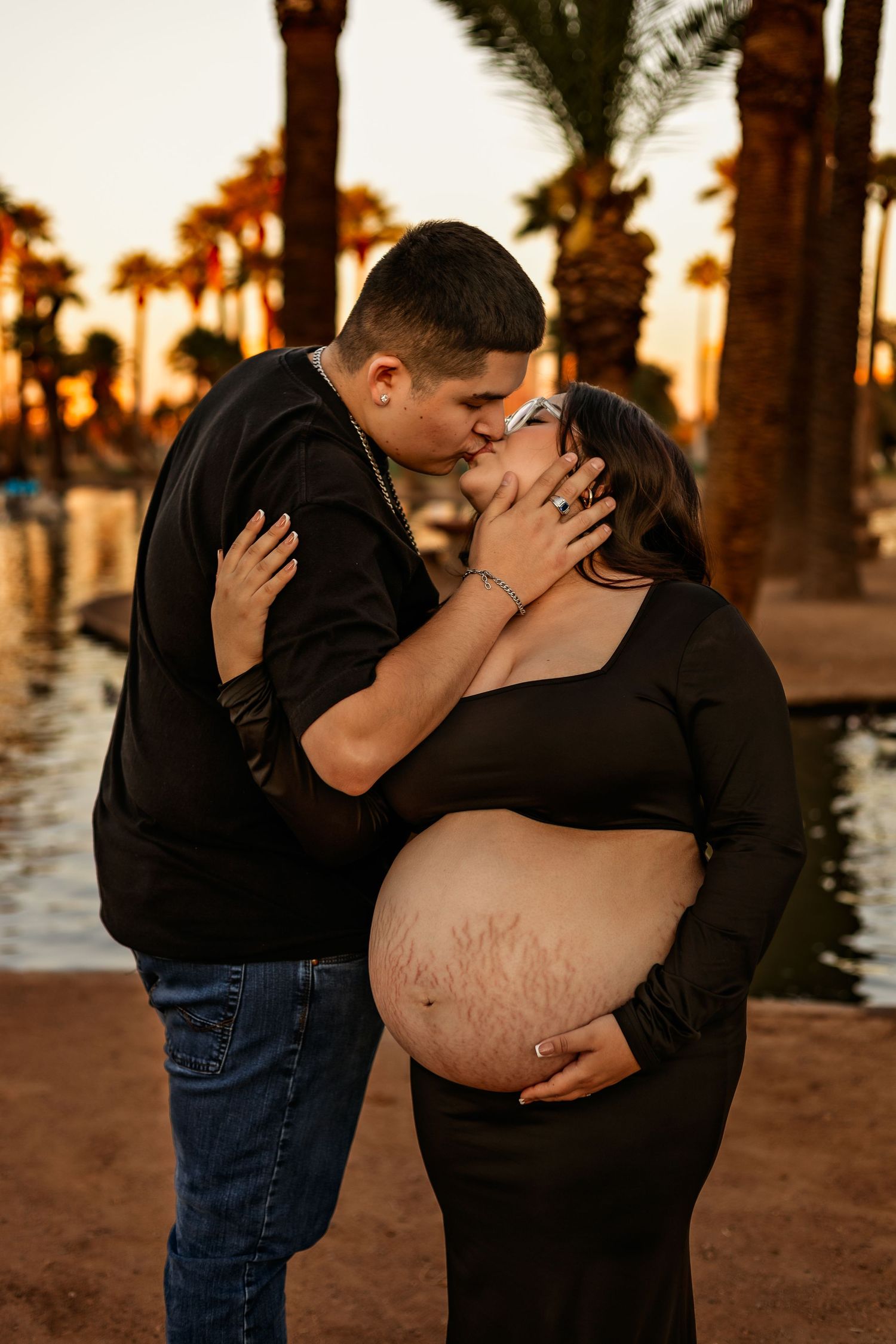 Romantic sunset maternity photo with couple embracing among palm trees.