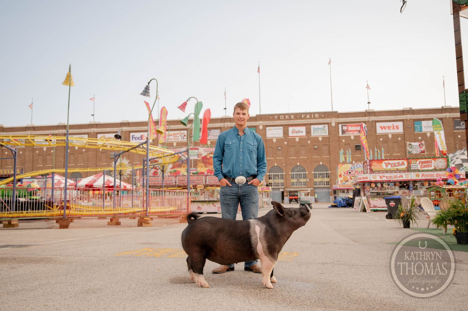 Black and white spotted show pig stands with handler at county fair grounds.