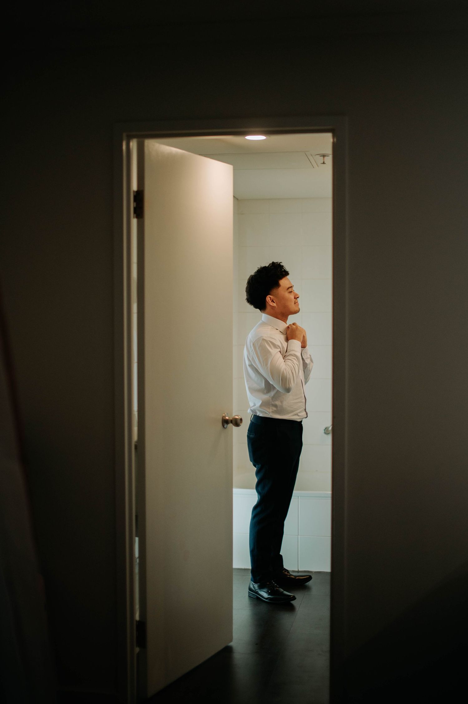 A silhouette of a person adjusting their tie while standing in a bright doorway.