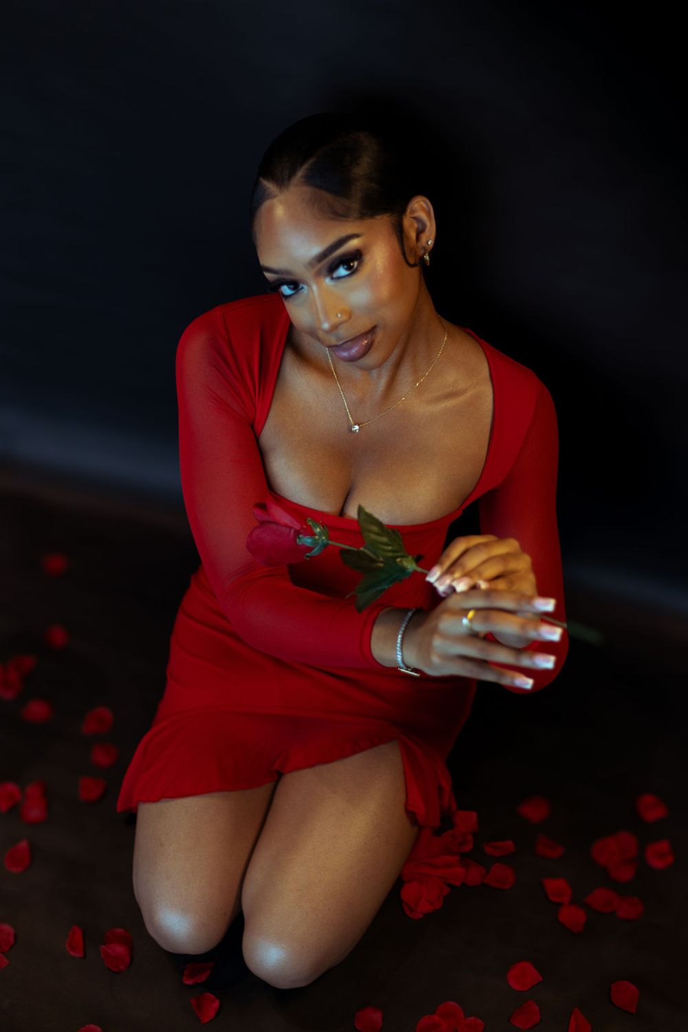 Glamour portrait with red dress and rose petals in dark setting.