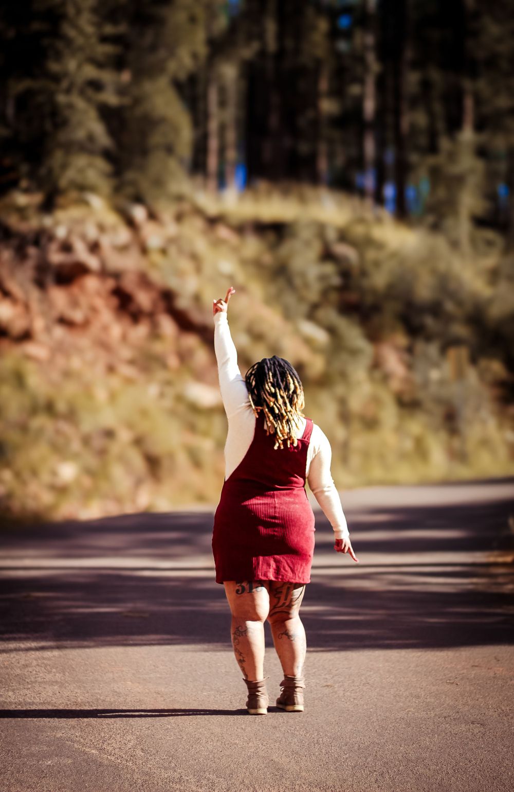 Person in red dress walking alone on mountain road with arm raised triumphantly.