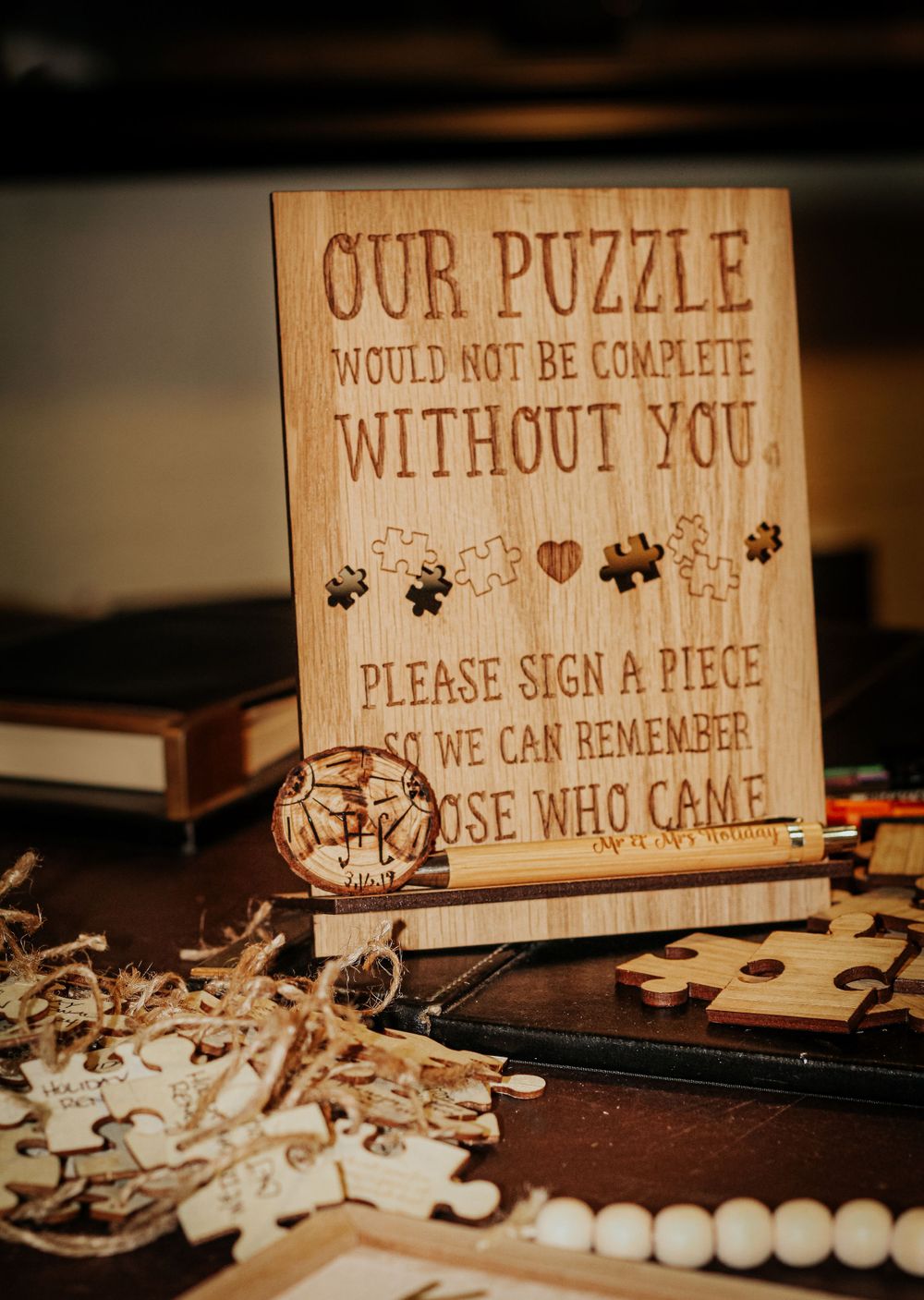Wooden wedding guest book sign with puzzle theme and scattered puzzle pieces.