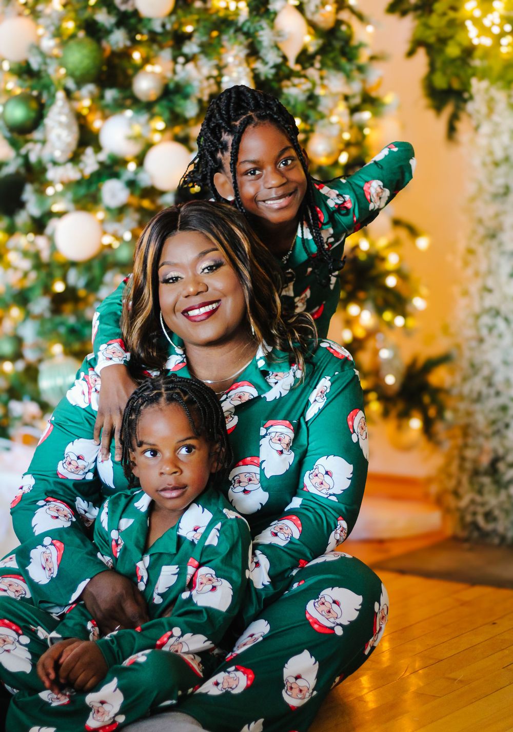 Family wearing matching Santa pajamas poses by Christmas tree with lights.