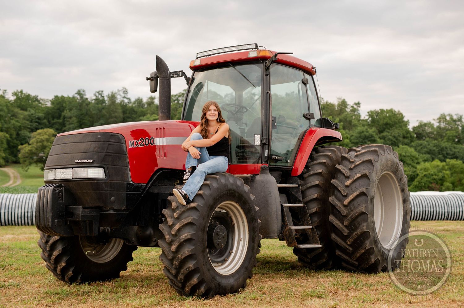 A casual farmland portrait featuring someone perched on a large red Case tractor.