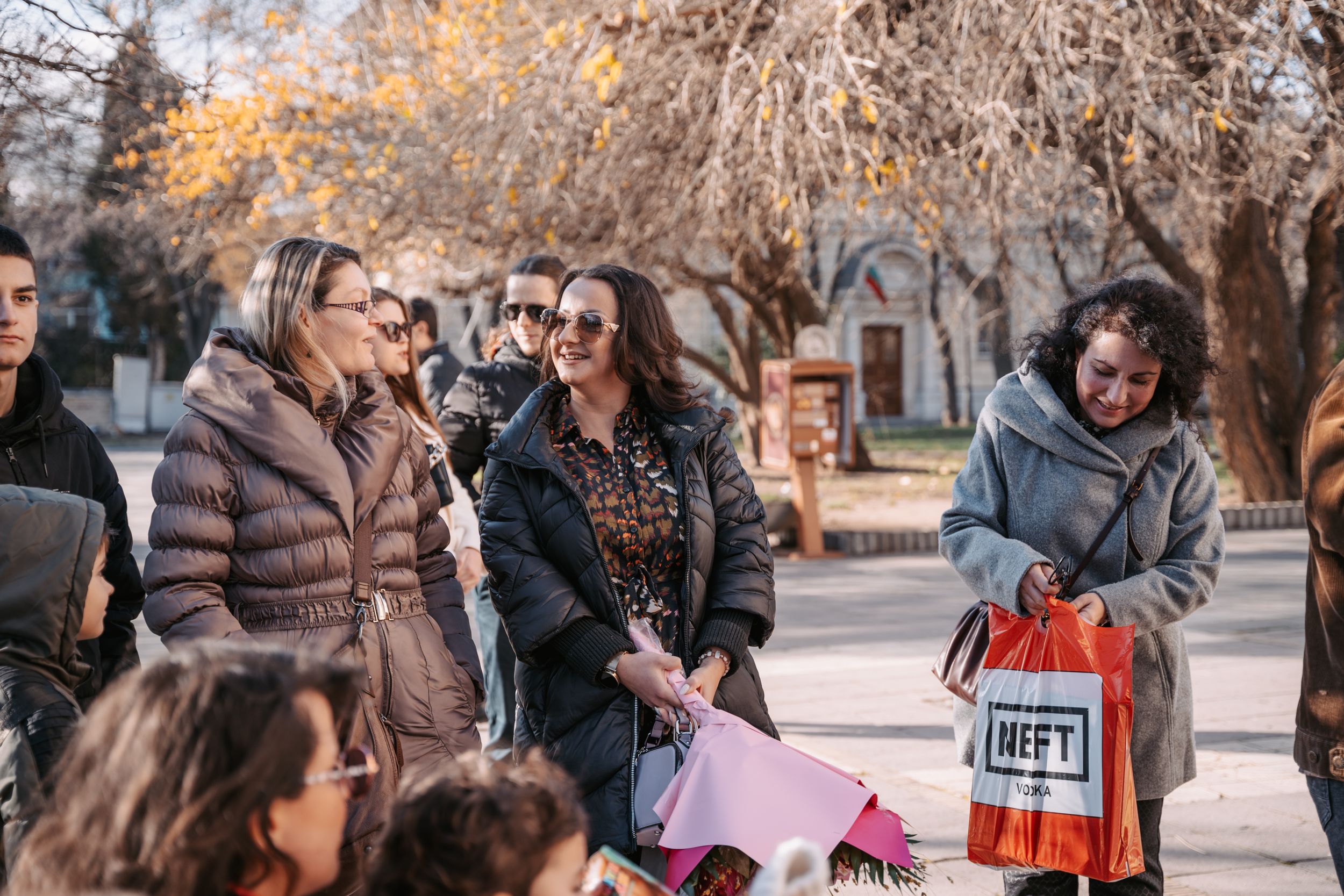 A group of people gathered outdoors on an autumn day for a social event.