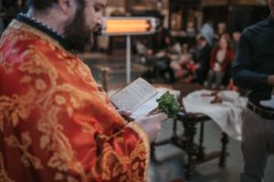 Orthodox baptism ceremony with priest in traditional red vestments performing sacred rituals.