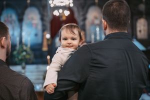 A small child in light colored clothing being held during a church ceremony.