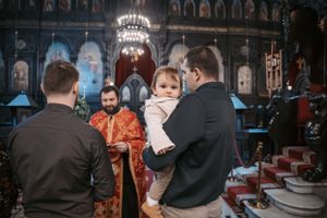 A church ceremony with a small child in white being held against ornate religious backdrop.