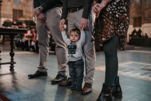 A small child standing among adults on a patterned floor in a church.