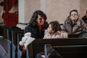 People seated in a wooden church pew during a religious service.