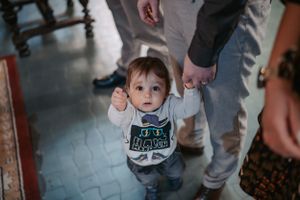 A toddler in casual wear walking while holding onto adult hands in a church.