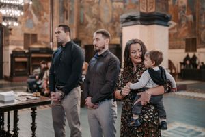 People standing in formal attire during a religious ceremony inside an ornate church.