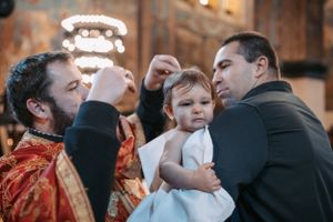 Baptismal ceremony taking place in an Orthodox church with attendees gathered around.