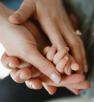 Close-up shot of two hands tenderly holding each other with soft natural lighting and neutral manicured nails.