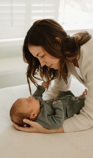 A tender moment between a mother and baby in warm natural light as they share a sweet connection on a white bed.