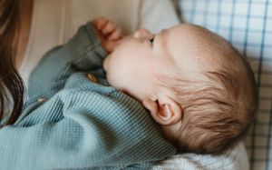 A small baby lying down in a blue sweater sleeps peacefully on a white and blue checkered surface.