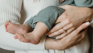 Close-up of tiny baby feet being gently held in adult hands while wearing soft gray clothing.