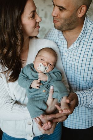 Loving couple gazing at their peaceful sleeping baby wearing a blue onesie and pacifier.