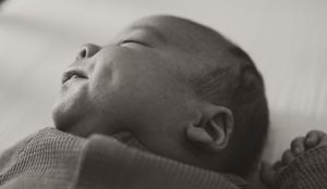 Close-up black and white photograph of a sleeping baby's face in profile against a soft background.