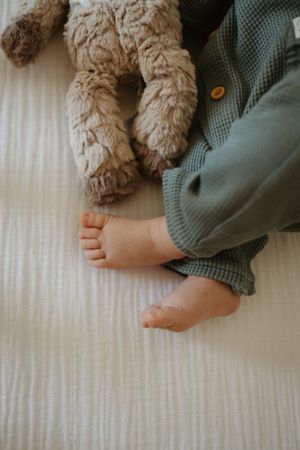 Baby's tiny bare feet next to a plush stuffed animal on white textured bedding.