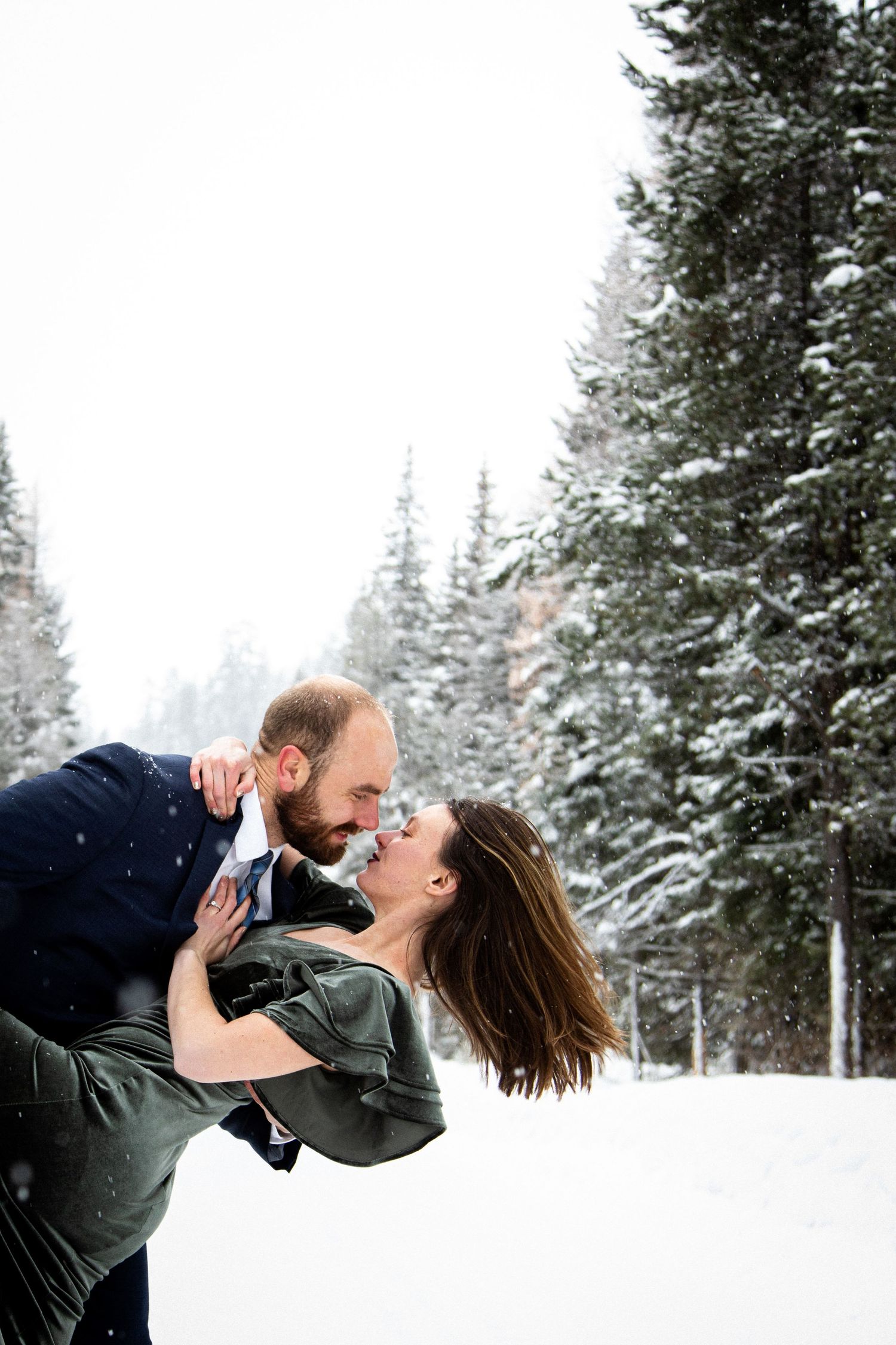 A romantic winter moment captured between two people in a snowy forest setting.