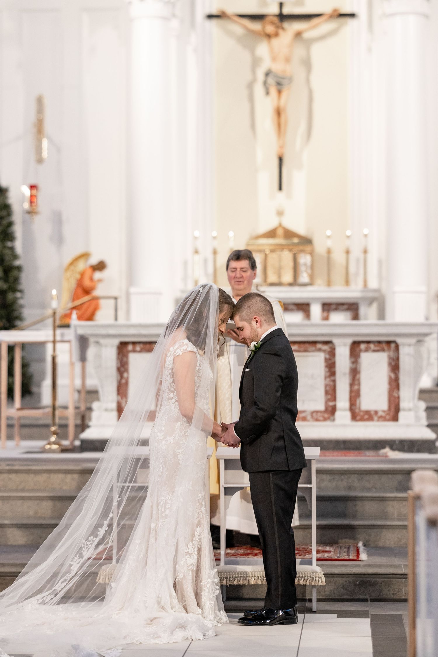 A traditional Catholic wedding ceremony in NoVa at the altar with a crucifix and ornate decorations in the background.